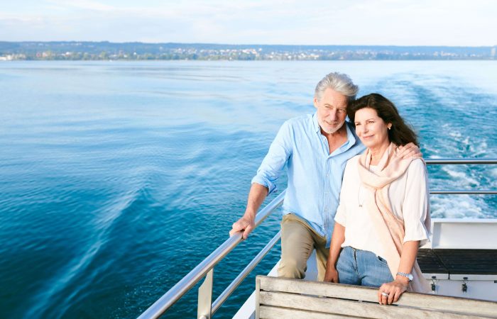 Ein älteres Paar steht auf Deck einer Fähre der BSB. Sie schauen nach vorne und genießen den Ausblick. Im Hintergrund ist der Bodensee zu sehen.